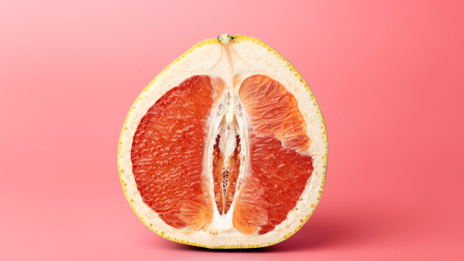 Der Länge nach halbierte Grapefruit. Der vertikal verlaufende Hohlraum zwischen den zwei sichtbaren Segmenten erinnert an eine Vulva. Der Kontrast zwischen dem saftig-roten Fruchtfleisch und den feinen weissen Häutchen und Häärchen verstärkt die Assoziation.